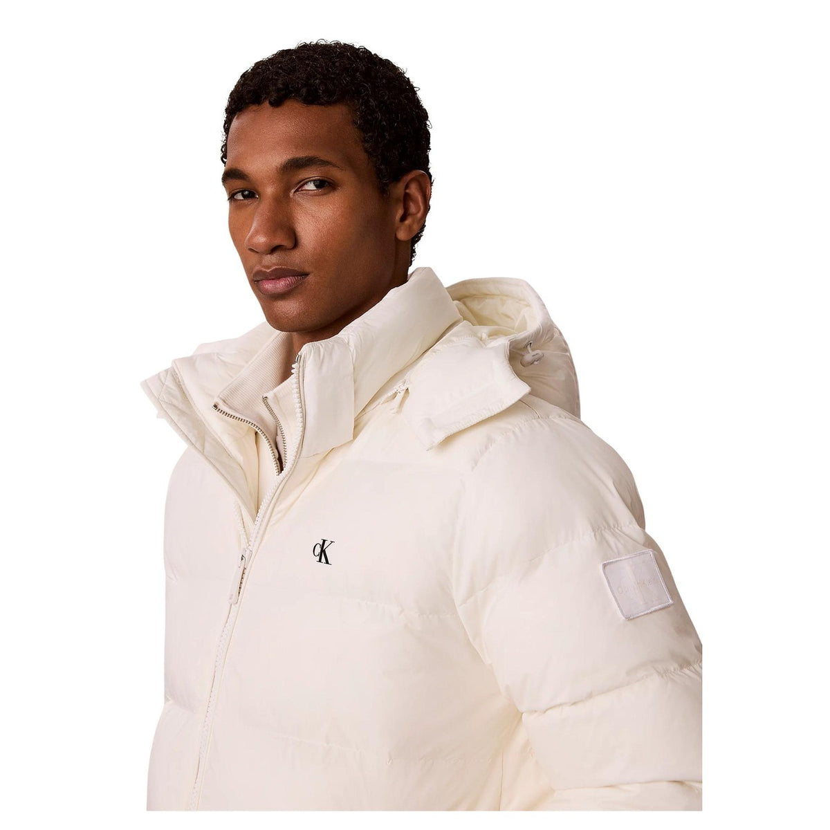 Piumino Calvin Klein uomo bianco LV04RG515G. Giaccone invernale pesante in poliestere riciclato ecosostenibile con logo cK ricamato, cappuccio, tasche laterali oblique e vestibilità regolare normal fit.