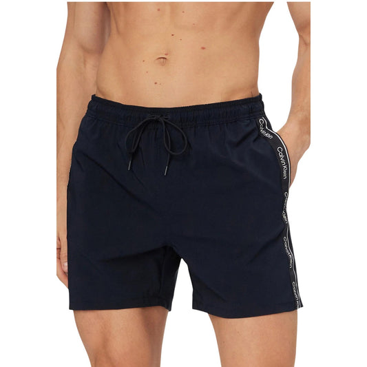 Boxer Mare CK Jeans Blu; Bande Laterali Logate. 10% Elastam per massima elasticità, poliestere riciclato, asciugatura rapida. Tasche laterali, vita con coulisse, fit regolare e sportivo Vista frontale