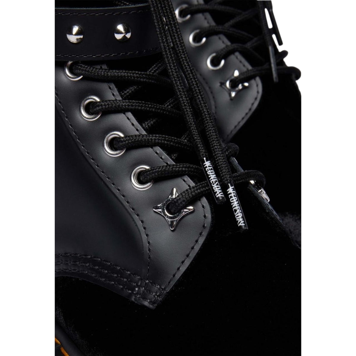 Anfibi Dr Martens Wednesday Addams 1460 neri. Stivaletti in velluto nero e pelle con cinturini decorativi, borchie argentate, ciondolo rosone, scritte ricamate viola, suola alta e impunture gialle.