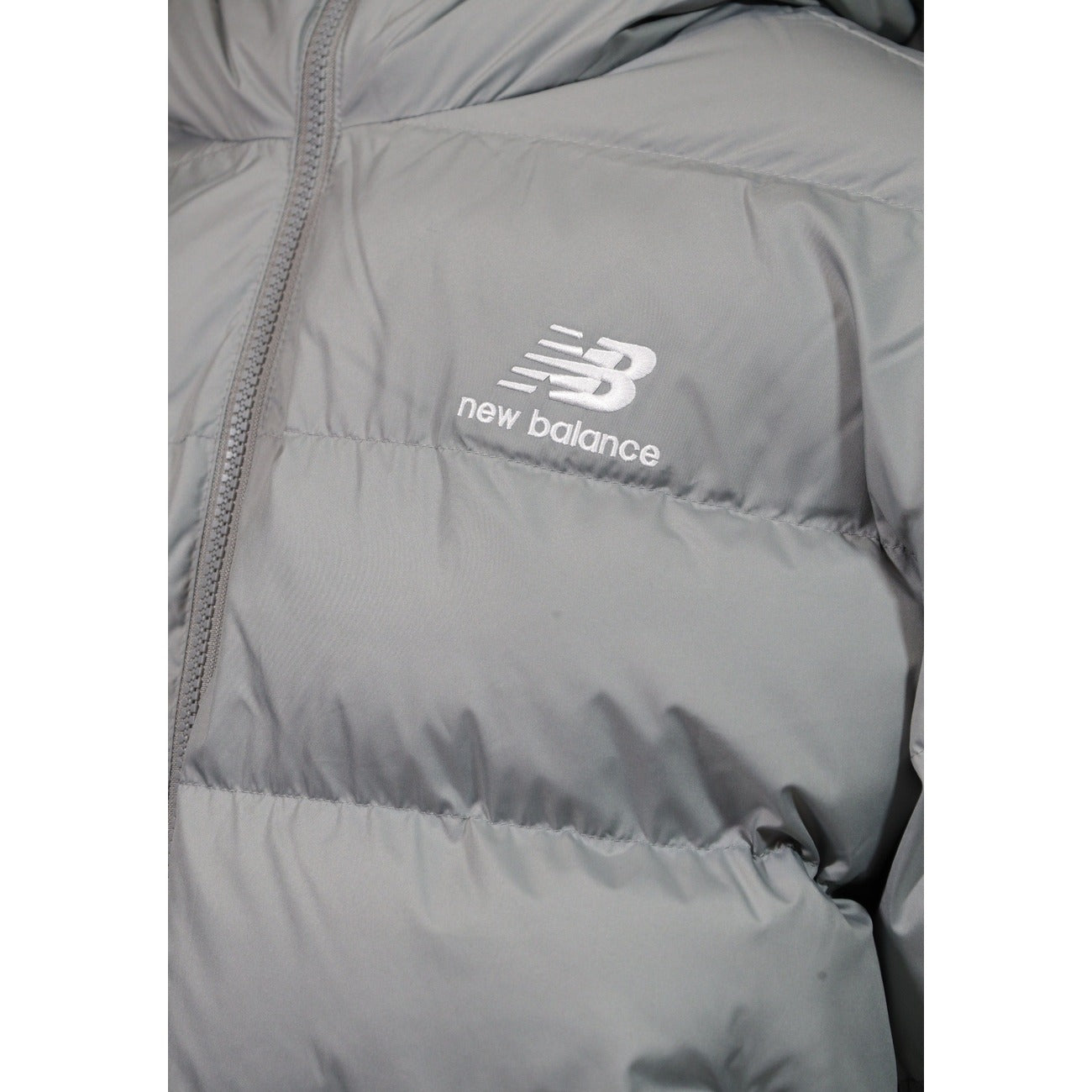 Piumino uomo New Balance grigio MJ62G17OYST. Giacca invernale pesante da uomo grigia con trapuntatura orizzontale, cappuccio, zip integrale, tasche con cerniera e logo ricamato, giubbotto casual sportivo da mezza stagione e freddo.