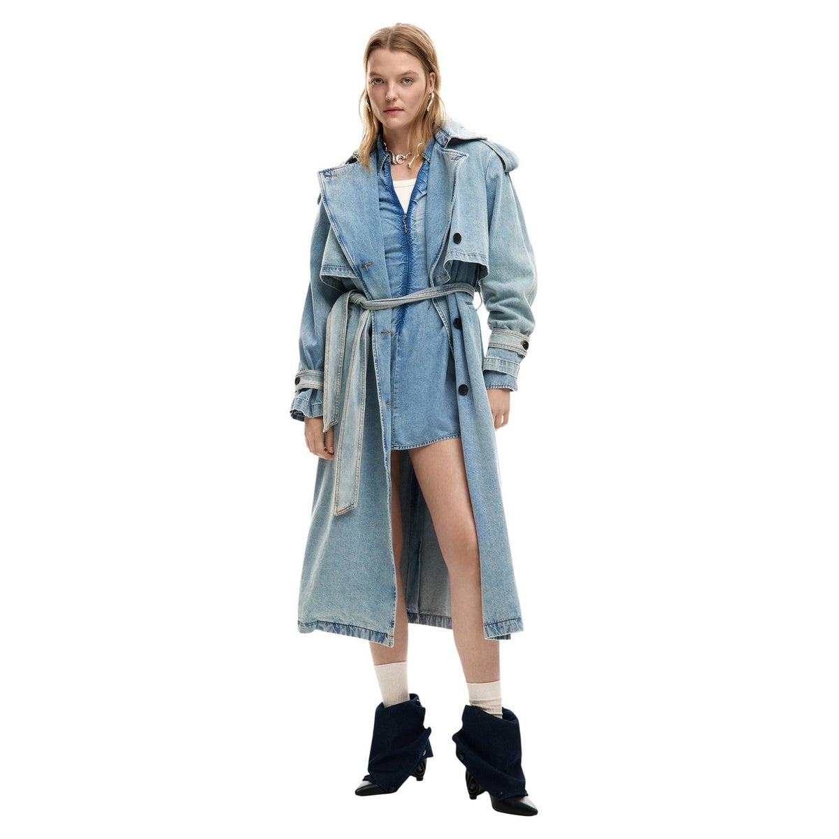 Giacca lunga stile trench in tessuto denim, con revers, chiusura con bottoni e cintura rimovibile. Vista frontale figura intera indossata da modella