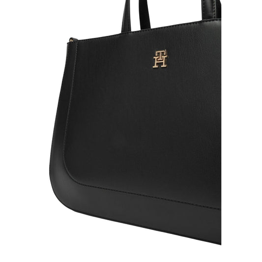 Borsa Tommy Hilfiger TH Glam Satchel; 100% Poliuretano liscio. Logo metallico, doppio manico e tracolla rimovibile. Borsa grande strutturata, ideale per ufficio e look formali. Colore nero vista frontale Dettaglio logo
