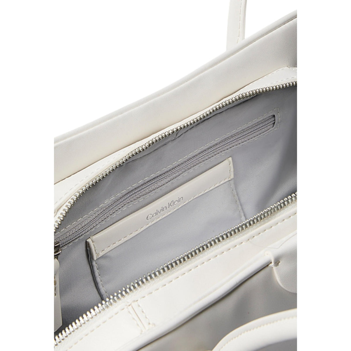 Calvin Klein Small Tote Bag; ecopelle morbida, scomparto centrale con zip, tasche magnetiche, ciondolo removibile. L'accessorio essenziale e organizzato per uno stile di vita contemporaneo. Colore bianco vista frontale Apertura