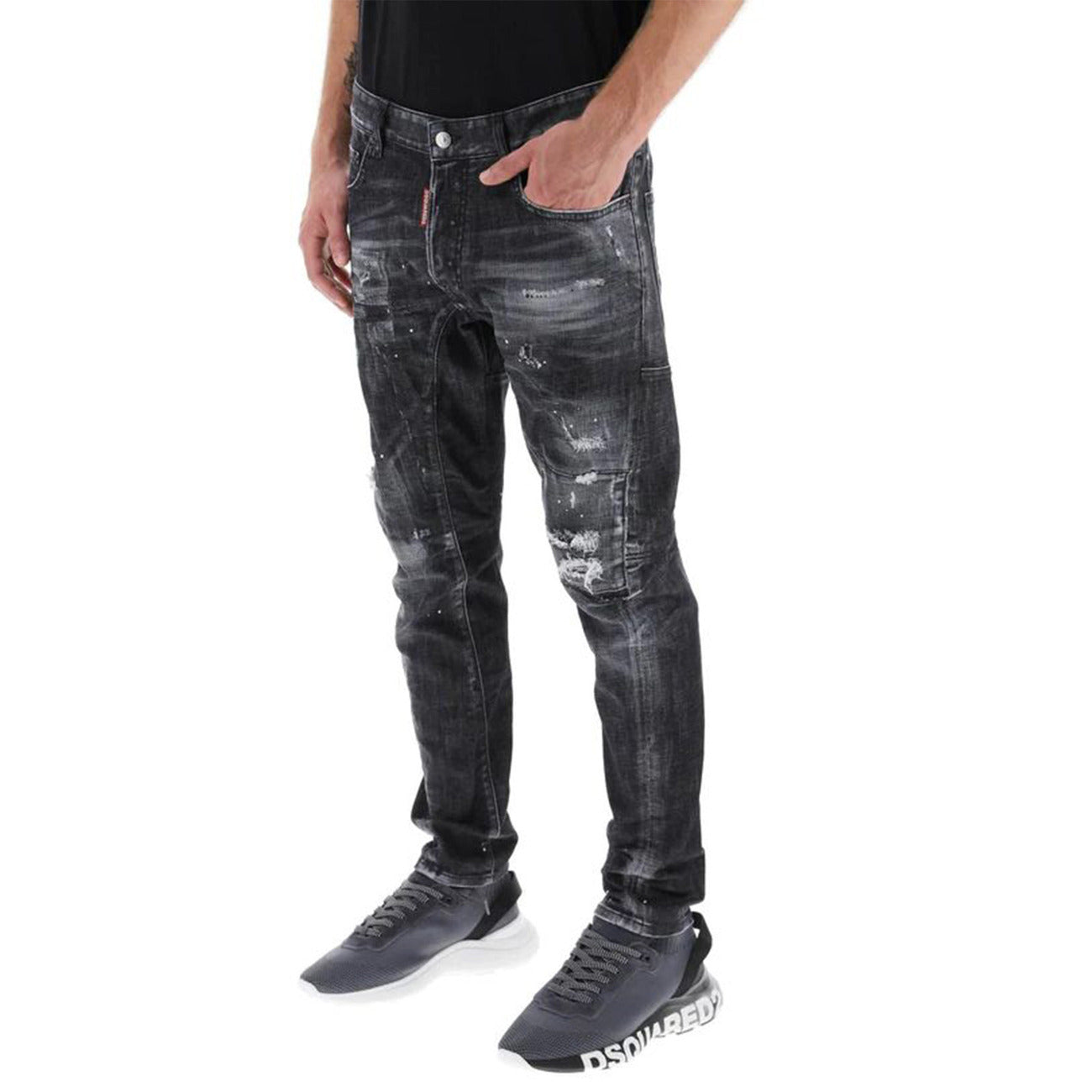 Jeans Dsquared2 Skater Fit; Black Wash Distressed. Dettagli con vernice, rammendi e patch rossa iconica. Taglio affusolato, denim di alta gamma, stile urban-premium. Vista frontale indossato da modello
