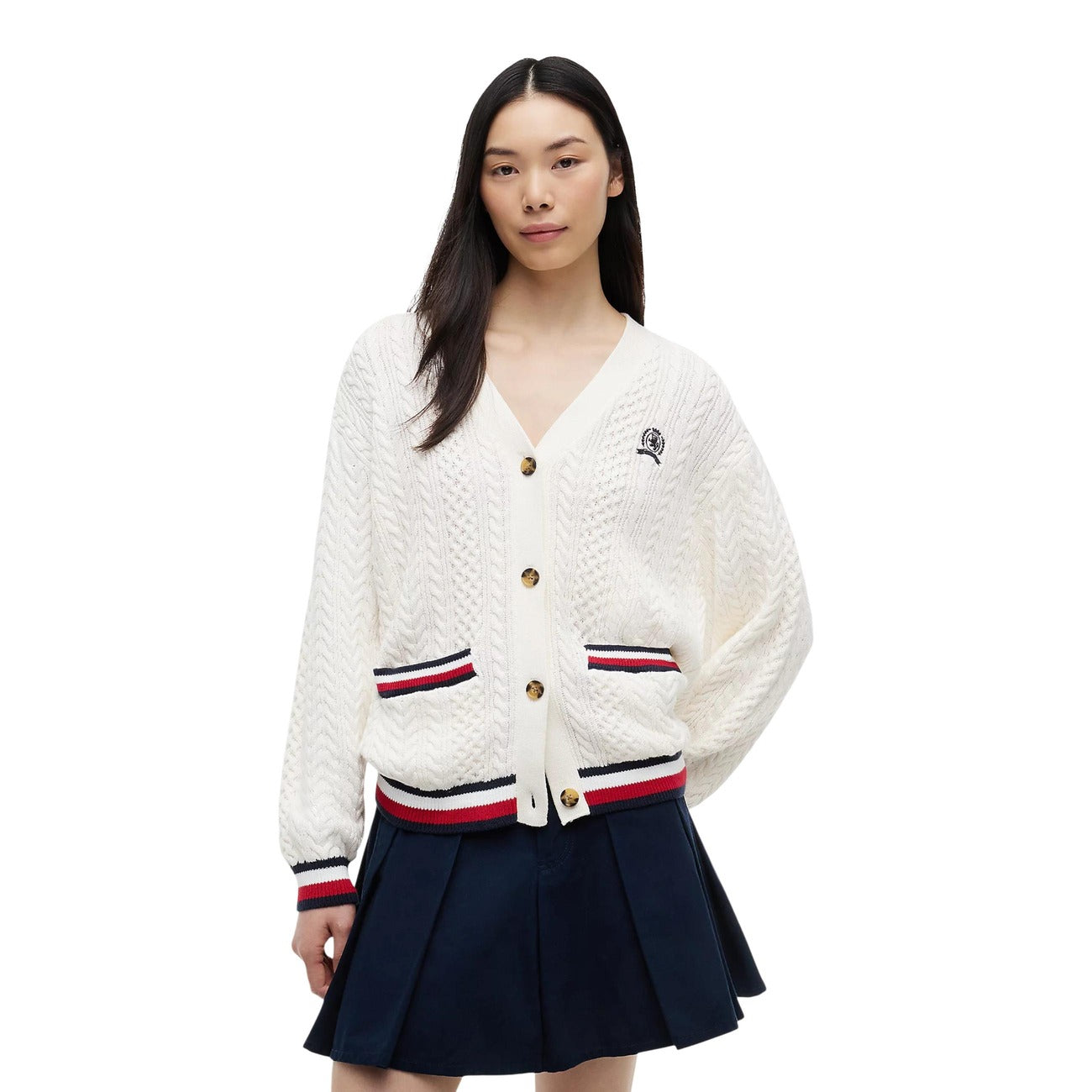 Cardigan Tommy Jeans donna bianco DW0DW22934. Maglione aperto in maglia intrecciata a trecce in 100% cotone biologico, scollo a V con bottoni, vestibilità oversize con stemma logo ricamato e finiture a righe stile college.