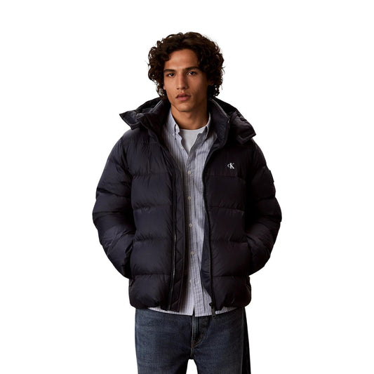 Giubbotto Calvin Klein Jeans uomo Dark Sapphire LV04RG515G. Piumino impermeabile blu scuro da uomo con cappuccio rimovibile, imbottitura vera piuma, doppia cerniera zip e dettaglio monogramma CK, giacca invernali da uomo.