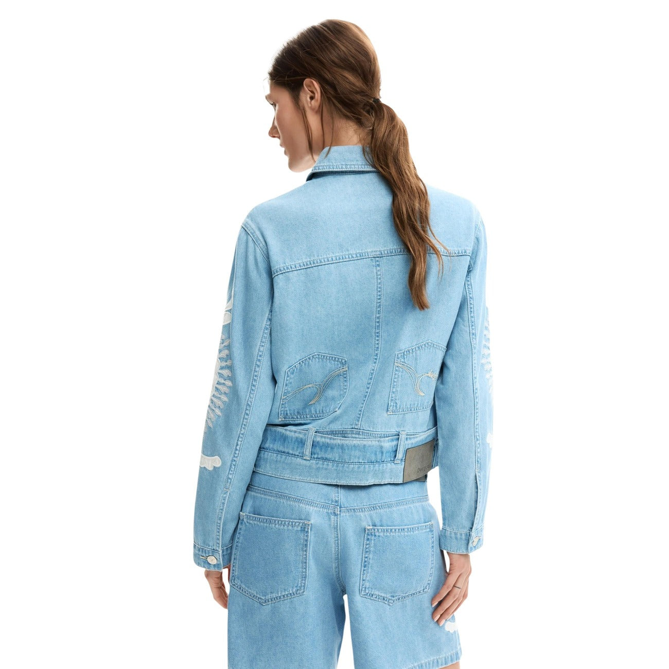 Giacca di jeans in cotone 100% con ricami in tonalità blu e design a taglio regular. Colletto a camicia e maniche lunghe con chiusura con bottone ai polsini. Chiusura frontale con bottoni e cuciture visibili. Indossata da modella vista posteriore 