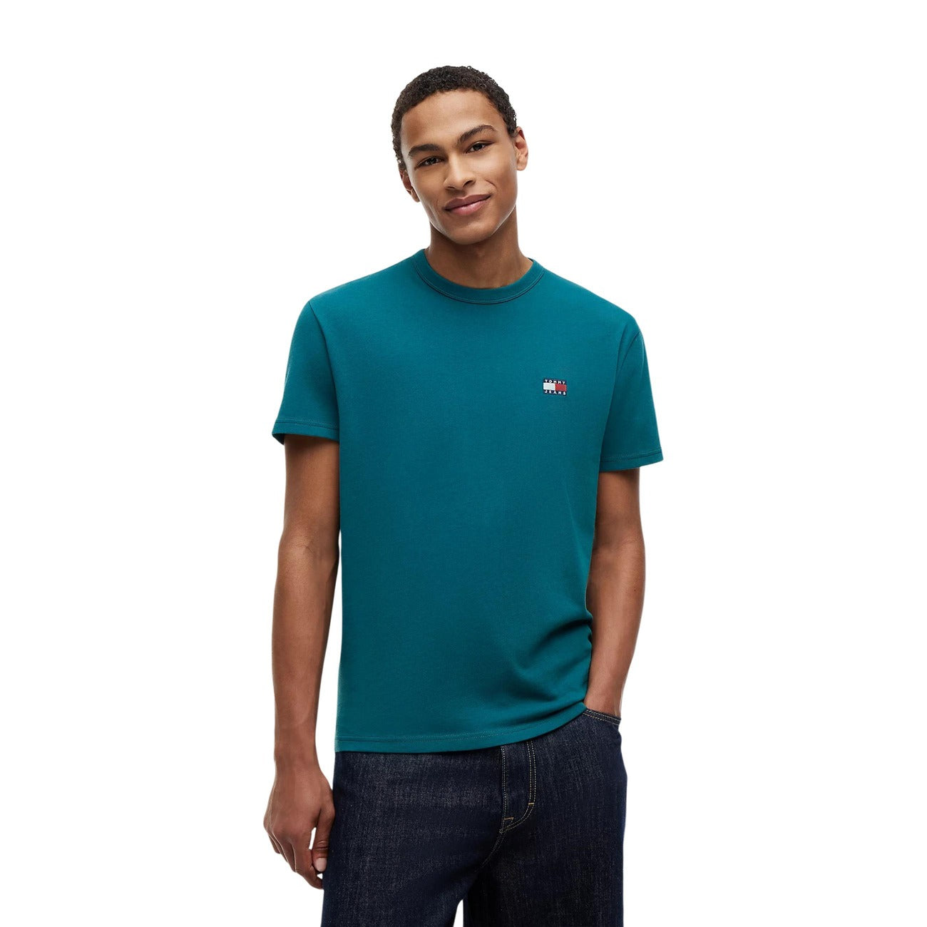 T-shirt Verde Tommy Jeans; Logo Badge Ricamato. 100% Cotone Rigenerato. Regular fit, girocollo classico, ecosostenibile. Il basic premium ideale per ogni outfit. Vista frontale 