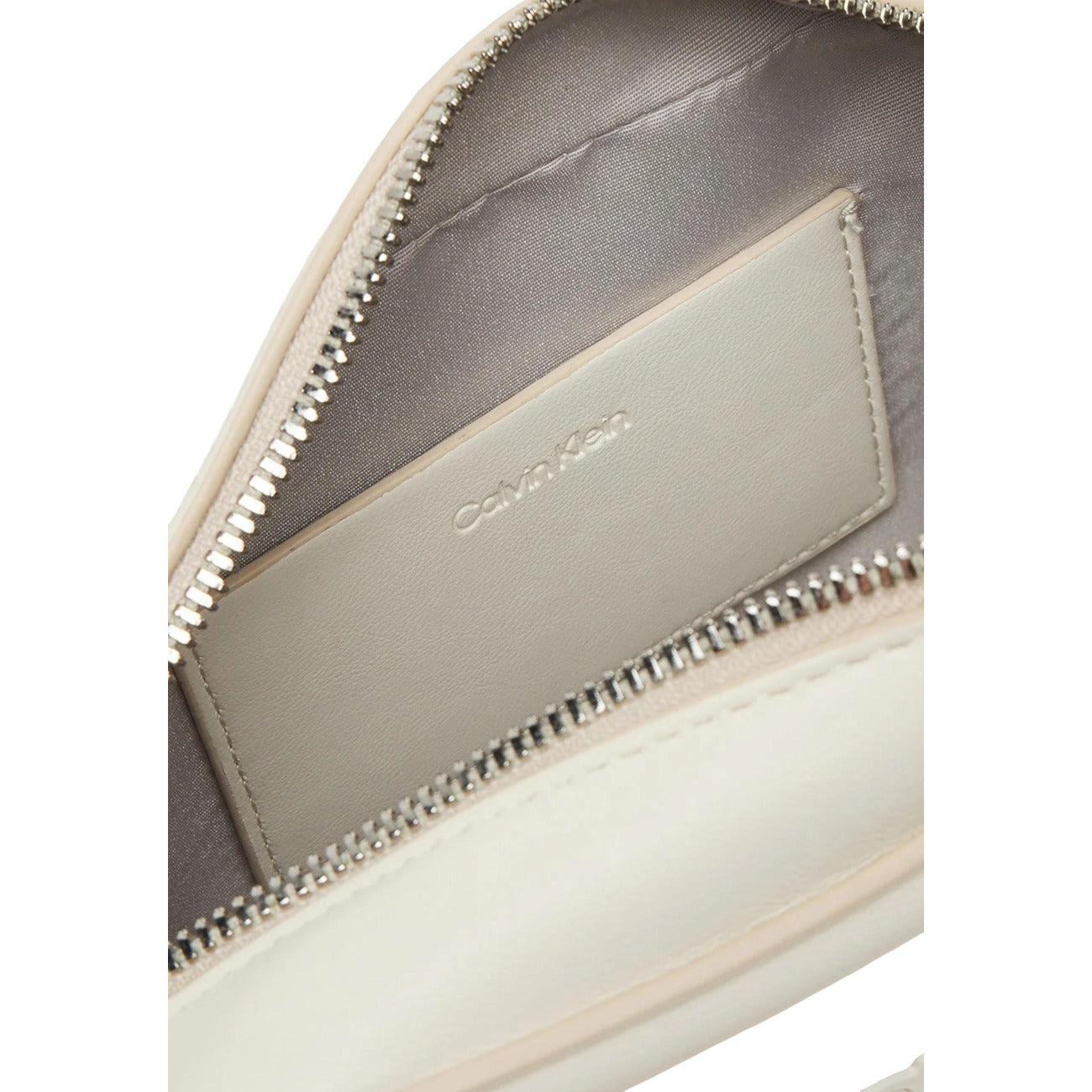 Borsa Camera Bag Calvin Klein; 100% Poliuretano Bianco. Logo CK embossed, chiusura con cerniera, tracolla regolabile. Misure: 20x13x5 cm. Design minimalista "all-white" per ogni stagione. Dettaglio cerniera 