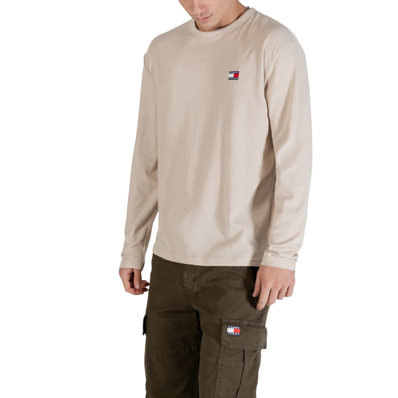 Maglia Tommy Jeans Beige Manica Lunga; 60% Cotone Rigenerato, 40% Poliestere Riciclato. Vestibilità regular, logo ricamato, scollo tondo. Tessuto morbido e sostenibile per la mezza stagione.