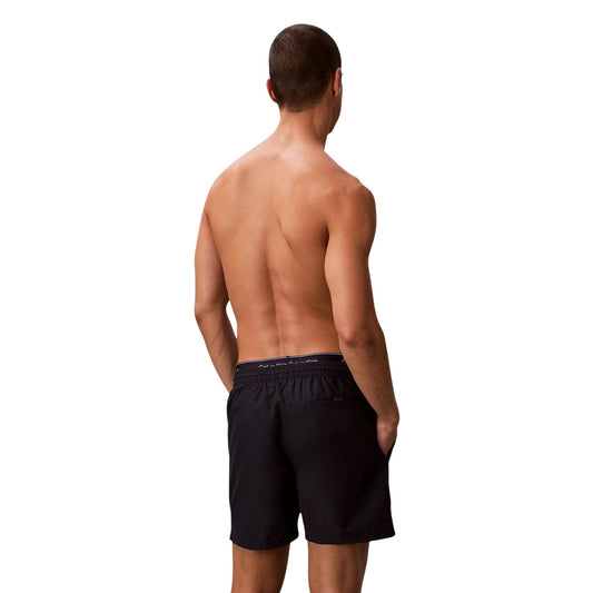 Boxer Mare CK Essentials; Tessuto Impermeabile. Doppia vita elastica logata, asciugatura rapida, lunghezza media. Tasca con velcro, slip a rete interno. Stile minimalista e funzionale per l'estate. Posteriore 