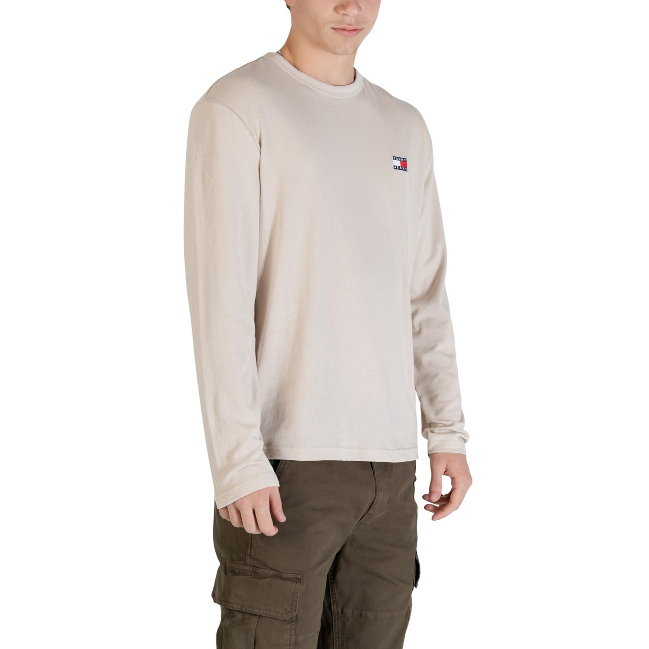 Maglia Tommy Jeans Beige Manica Lunga; 60% Cotone Rigenerato, 40% Poliestere Riciclato. Vestibilità regular, logo ricamato, scollo tondo. Tessuto morbido e sostenibile per la mezza stagione. Vista frontale laterale 