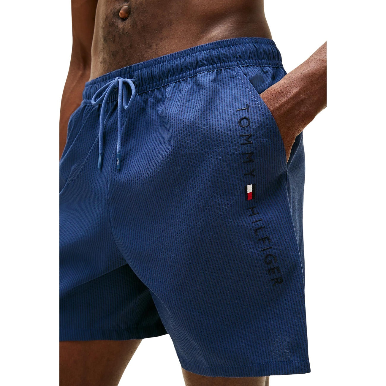 Costume Shorts Tommy Hilfiger; Righe Ithaca tono su tono. Tessuto tecnico, tasca con zip laterale, dettagli iconici sul retro. Lunghezza media, stile nautico elegante e funzionale.