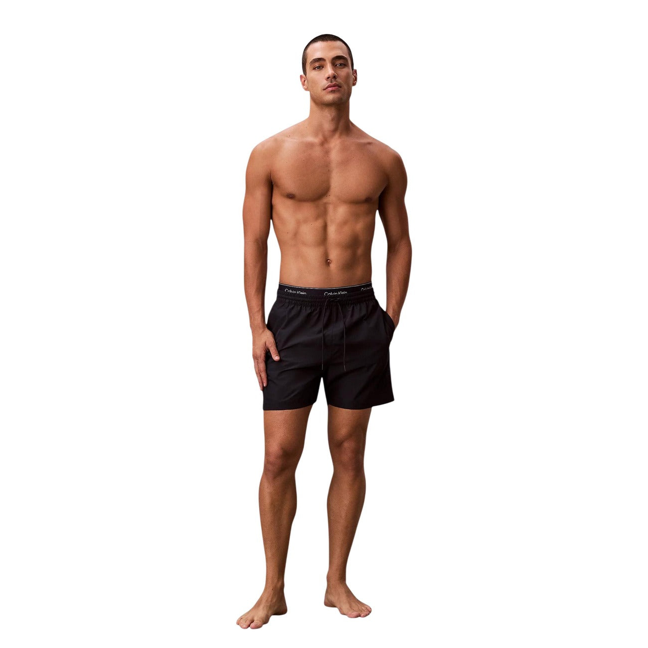 Boxer Mare CK Essentials; Tessuto Impermeabile. Doppia vita elastica logata, asciugatura rapida, lunghezza media. Tasca con velcro, slip a rete interno. Stile minimalista e funzionale per l'estate. Figura intera 