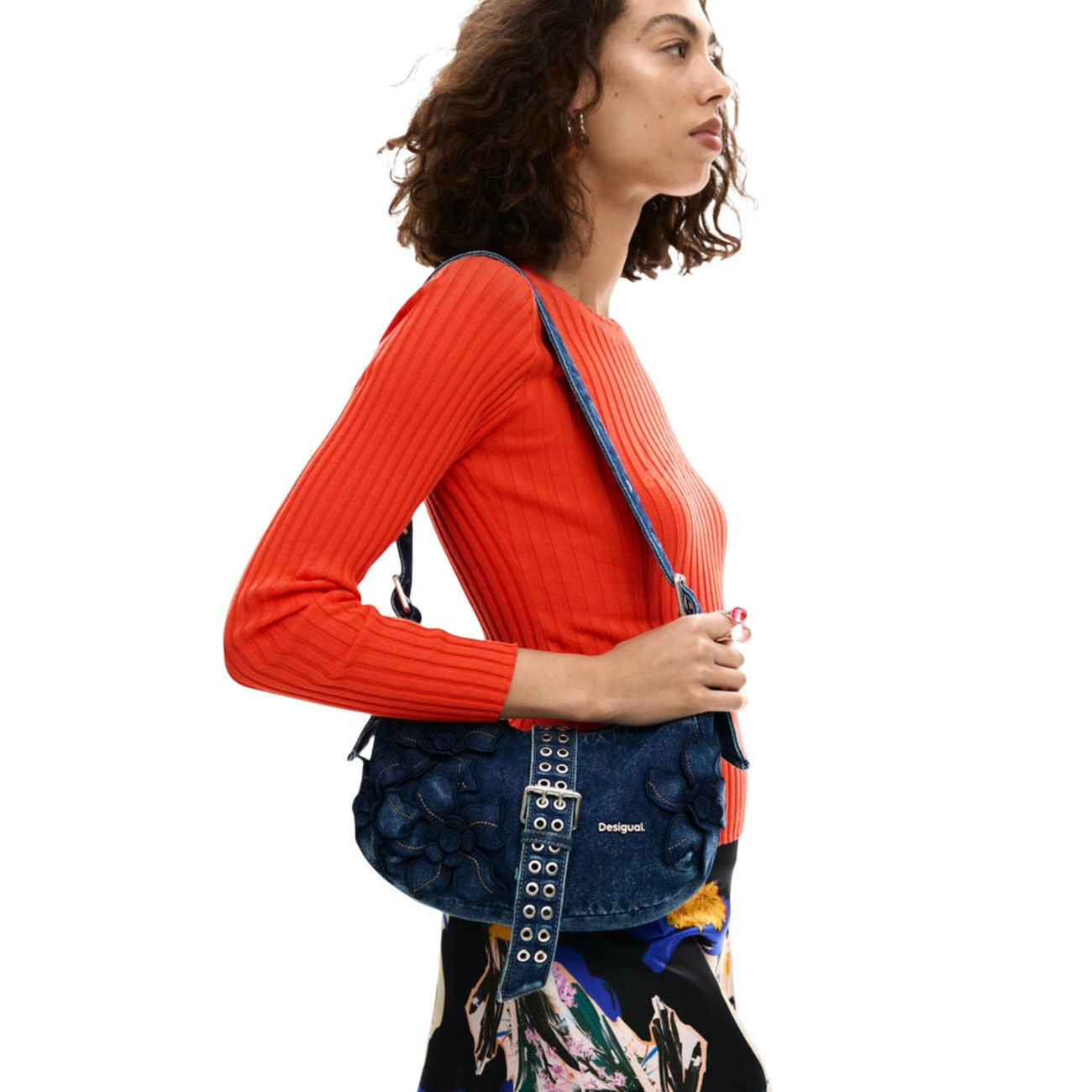 Borsa a tracolla realizzata in denim blu con struttura semirigida, patta superiore e cuciture a contrasto. Tracolla regolabile e chiusura principale con magnete nascosto. Tasca posteriore con cerniera visibile.
Indossata da modella 