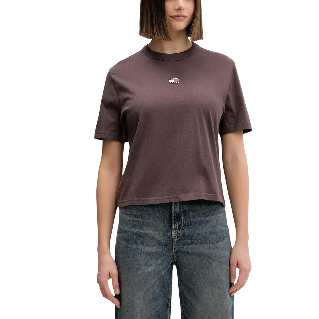 T-shirt Donna Tommy Jeans Boxy Cropped; 100% Cotone. Spalle scese, logo badge sul petto, taglio corto. Maglia donna fresca e di tendenza per la PE26. Colore Marrone
