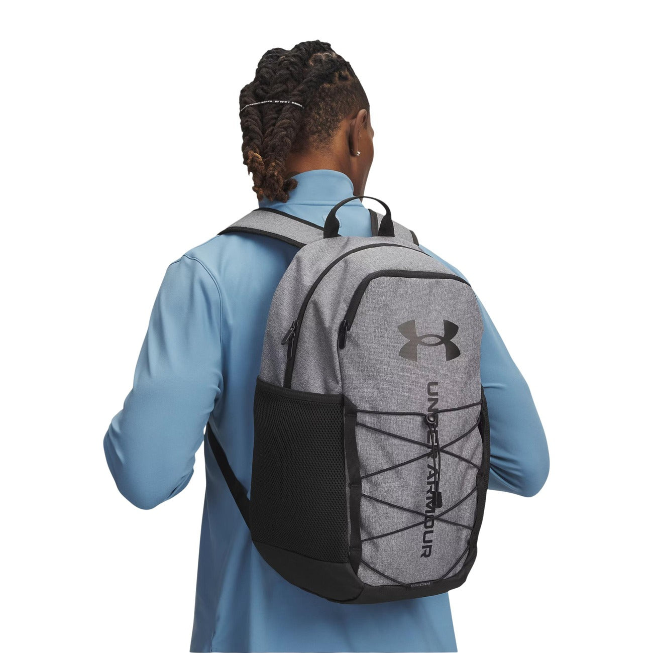 Zaino Uomo Grigio Under Armour Hustle Sport 6.0; Struttura 100% poliestere resistente con chiusura a zip e logo frontale. Sistema elastico porta-accessori, tasche laterali in rete e spallacci comfort regolabili, stile sportivo 4 stagioni. Indossato da modello 
