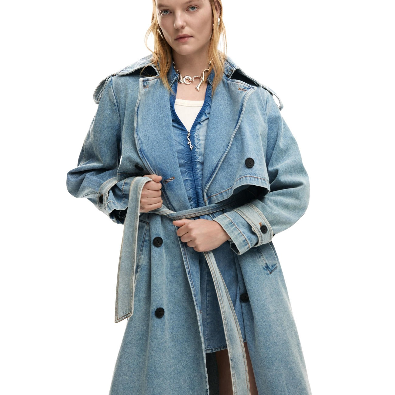 Giacca lunga stile trench in tessuto denim, con revers, chiusura con bottoni e cintura rimovibile. Vista frontale indossata da modella 